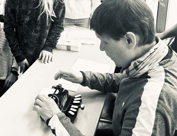 Unsere Projektmitarbeiterin erklärt den Kindern die Brailleschrift und schreibt auf ihrer Punktschriftmaschine. Die Kinder lauschen ihr und dem hämmernden Geräusch der Maschine ganz aufmerksam.
